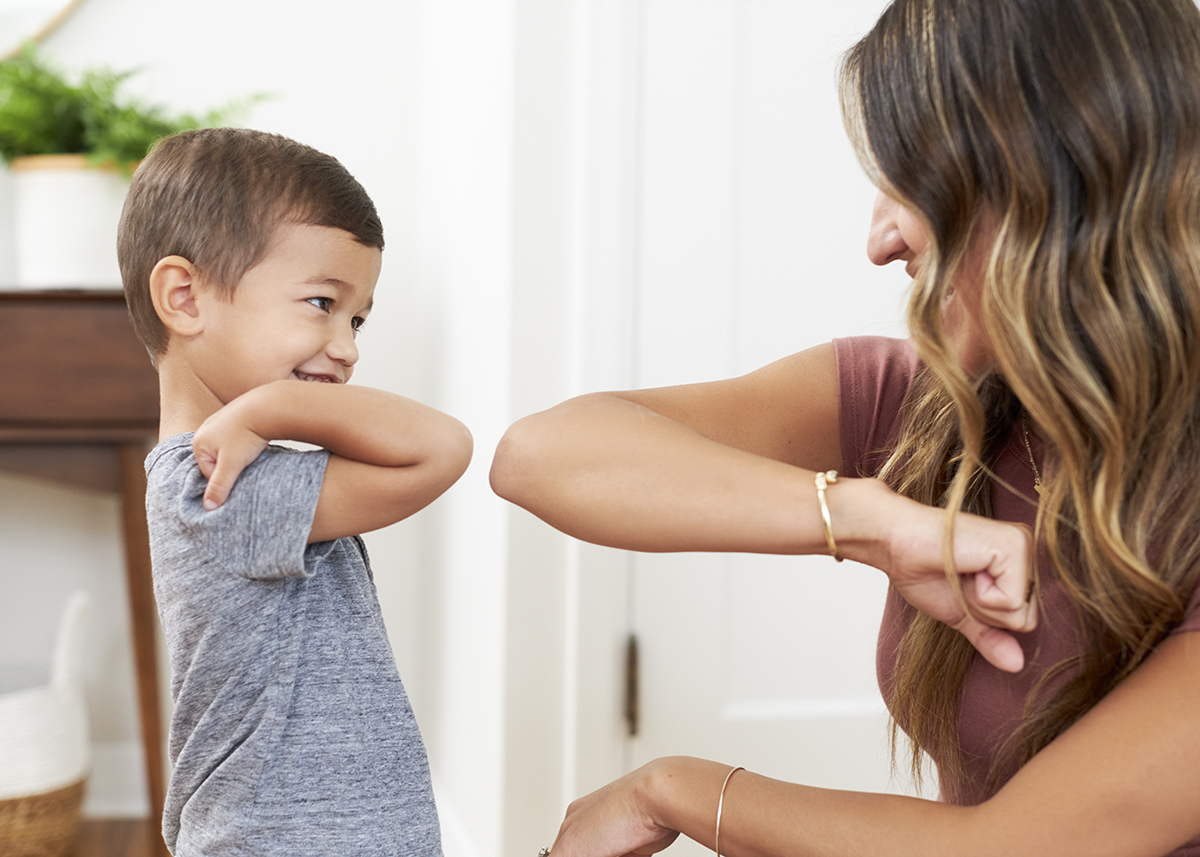 Woman touching elbows with a young child while smiling and looking at each other