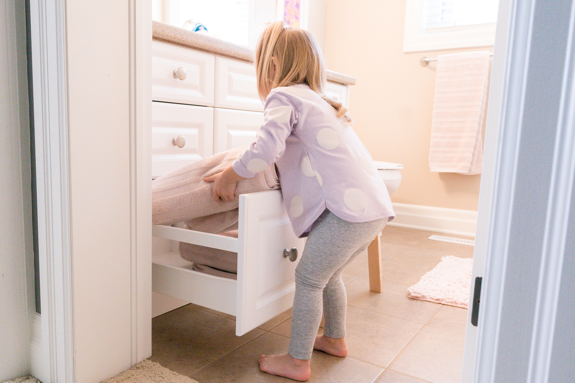 Young child putting towels away in a drawer in a bathroom
