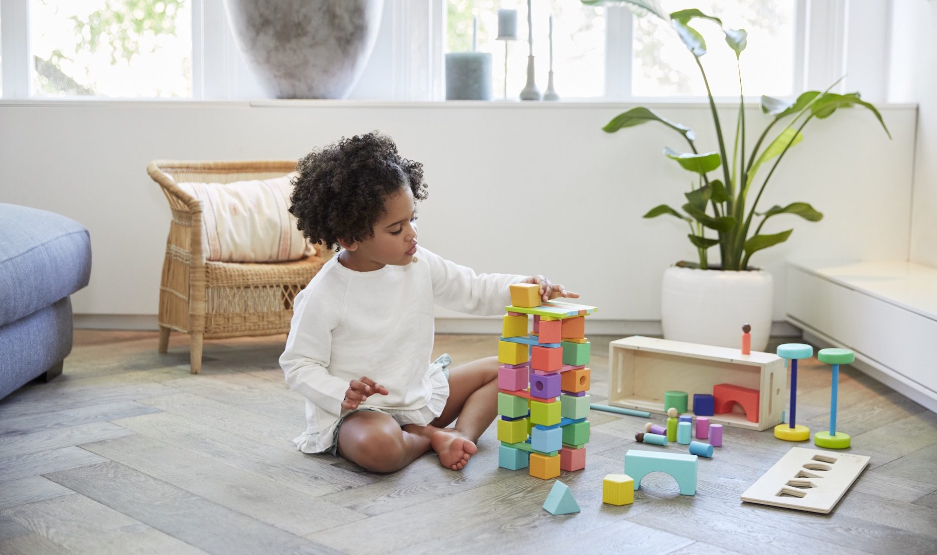 Young child sitting on the floor building a tower with The Block Set by Lovevery