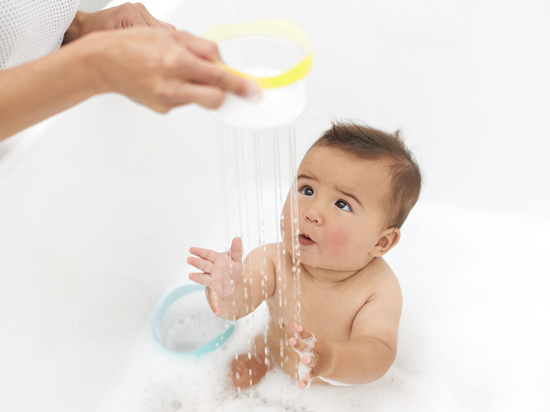 Toddler in a bathtub holding the Opposite Balls by Lovevery