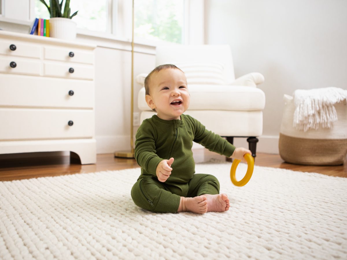 Baby sitting up on a rug with a toy