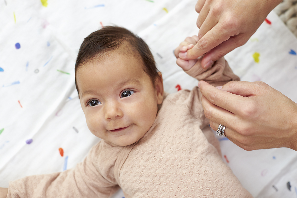 Baby laying down grabbing on to a woman's finger