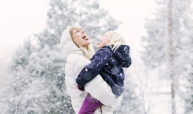 Mother collects snowflakes on her tongue with her daughter.