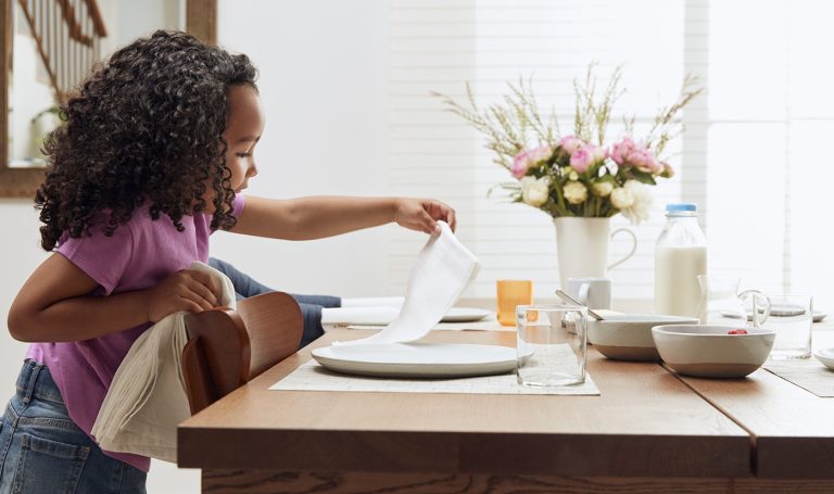 Little girl sets the table for a meal.