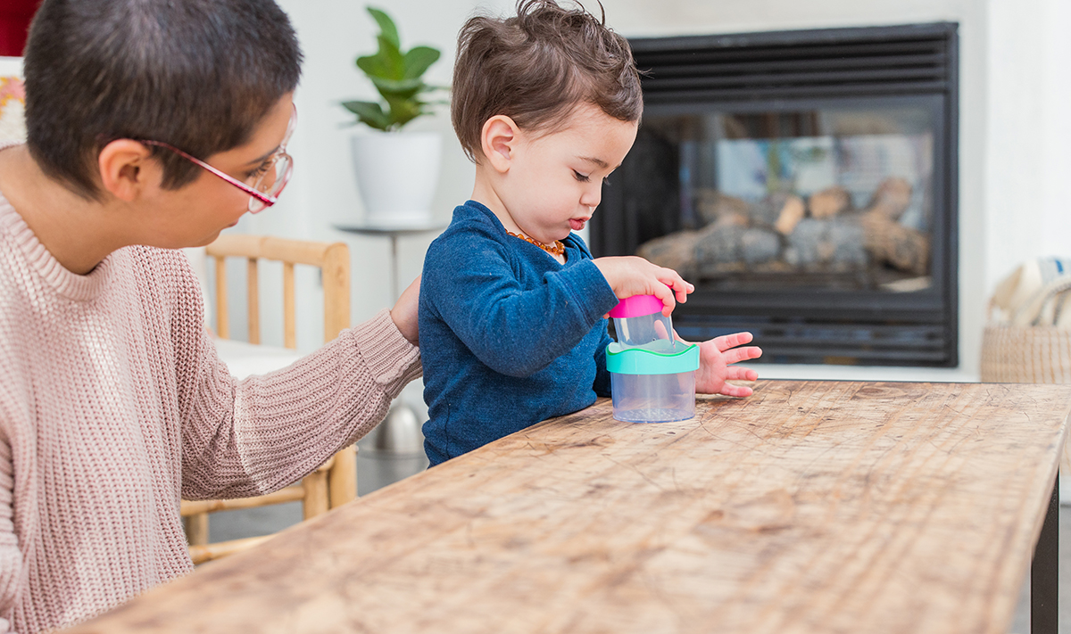 Toddler sitting at a table stacking the Nesting Stacking Drip Drop Cups by Lovevery