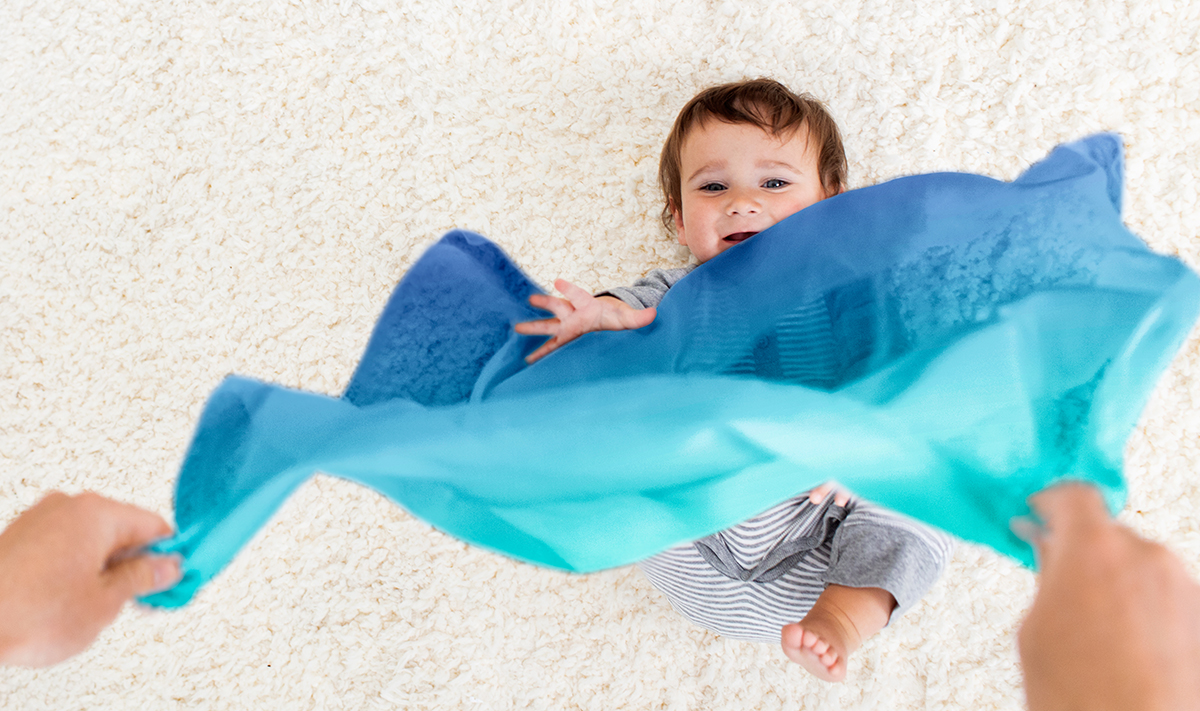 Woman hanging a scarf in front of baby who is laying on the floor
