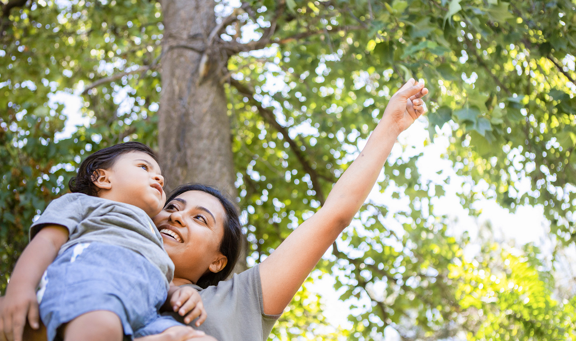 Mother speaks to her child as sunlight filters through the tree overhead.