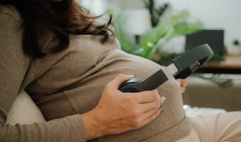 Mother holds headphones to her pregnant belly.